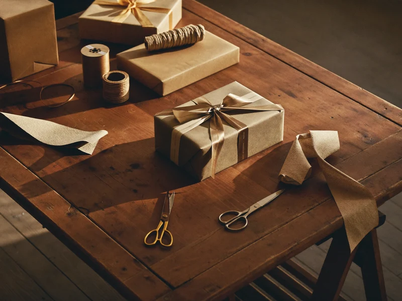 Geschenktisch mit Boxen, Papierrollen, Bändern und Schere in weichem Fensterlicht